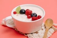 pexels-photo-5946069-5946069 Top view of a white cup filled with yogurt and assorted berries on a pink background.